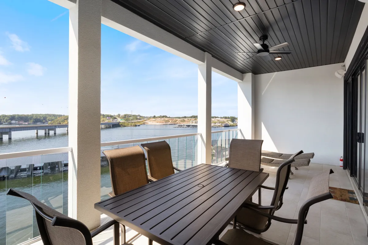 An inviting patio features a dining table and chairs set under a ceiling fan, all overlooking the water. The scene is perfect for socializing, dining outdoors, or relaxing with loved ones while taking in the serene lake view.