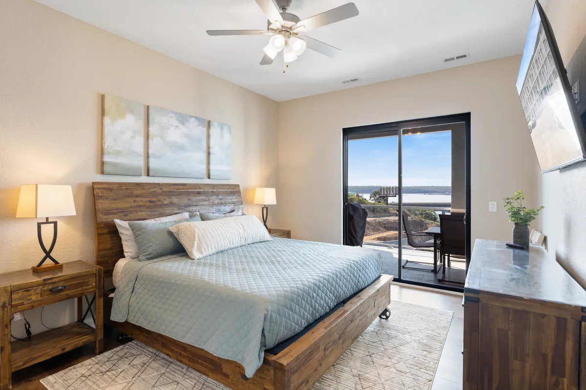 A serene king suite featuring a comfortable bed with a plush headboard, nightstands on each side, tasteful artwork above, and a sliding glass door that fills the room with natural light. The decor is soothing and modern, creating a peaceful atmosphere for relaxation.
