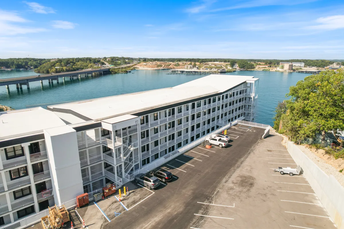 A waterfront view of the modern building facade, with a parking lot in the foreground. The serene lake and the building’s sharp lines evoke a sense of place—Lake of the Ozarks—with direct access to water activities and scenic views right at your doorstep.