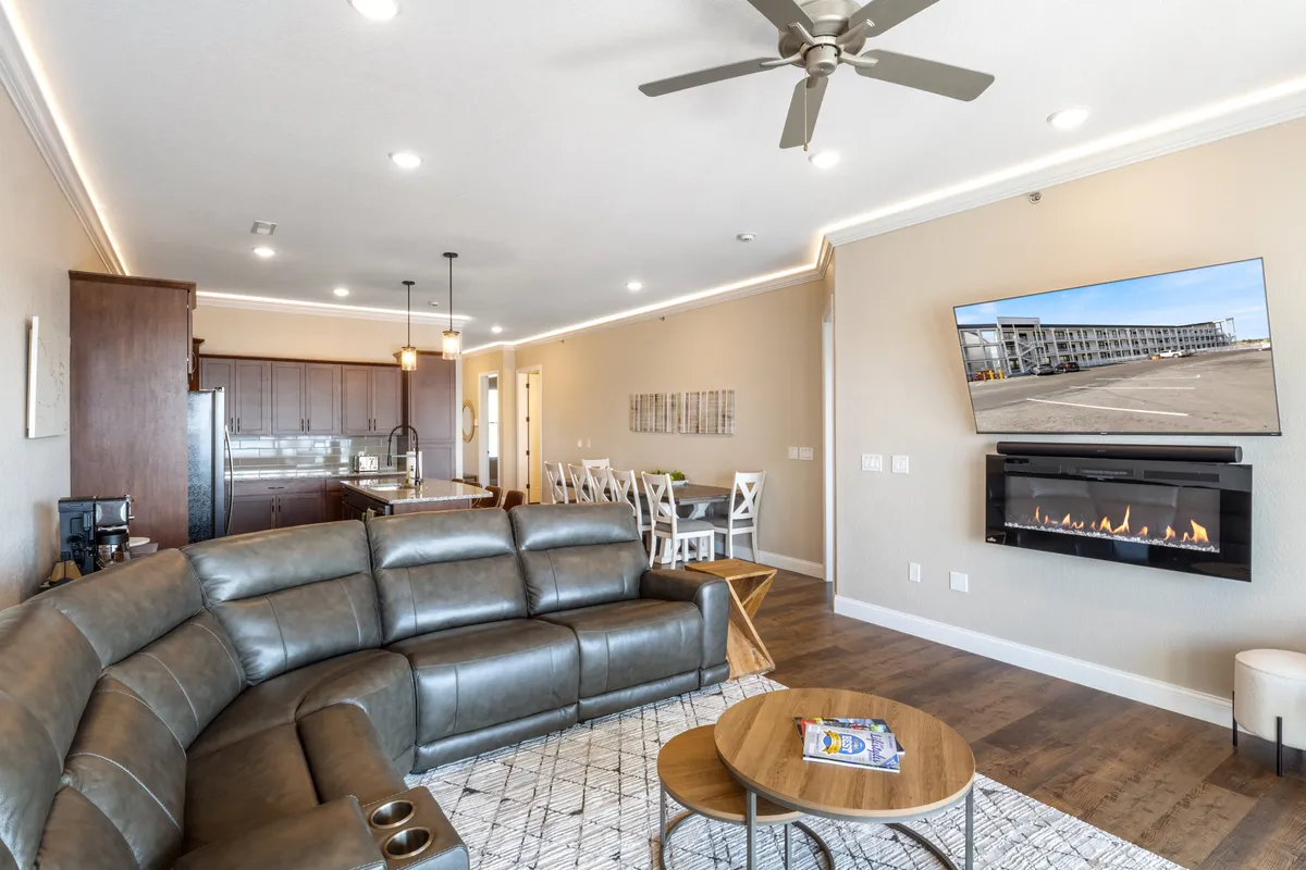 A cozy living space featuring a leather sectional sofa, a fireplace, and a wall-mounted TV. The adjacent dining area is visible, framed by modern décor and warm lighting, creating an atmosphere ready for both lively gatherings and quiet evenings.
