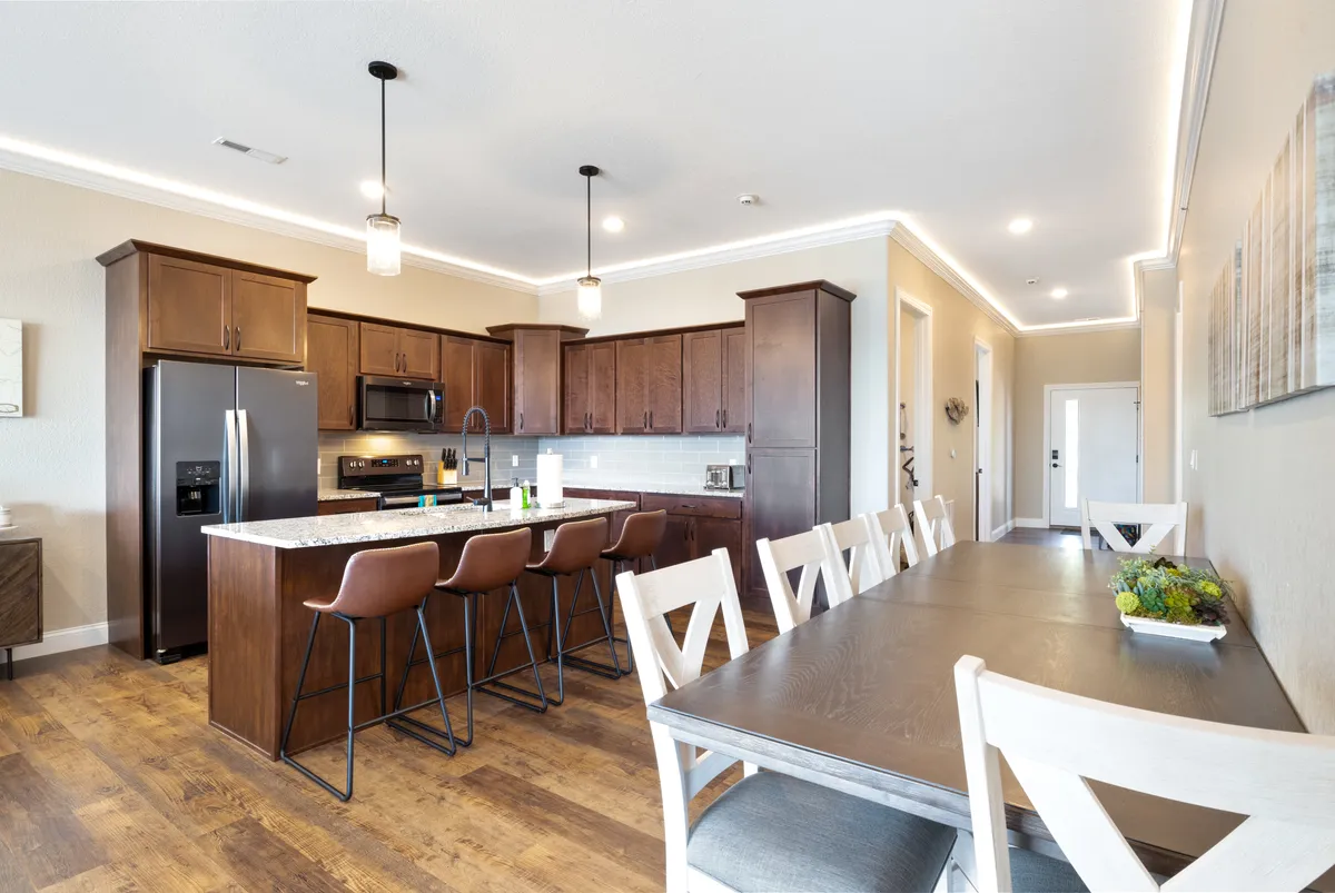A bright, open-concept kitchen and dining area featuring a kitchen island, adjacent dining table, modern bar stools, and pendant lighting. The layout emphasizes the seamless transition between cooking and dining, with ample natural light creating an inviting atmosphere for family meals or entertaining guests.