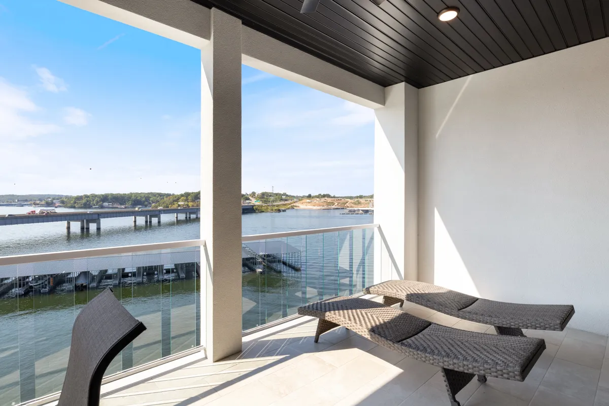 An inviting outdoor lounge area with plush chairs facing the water, and a distant bridge visible. The mood is peaceful and contemplative, ideal for quiet moments or simply enjoying the boat-filled lake scene.
