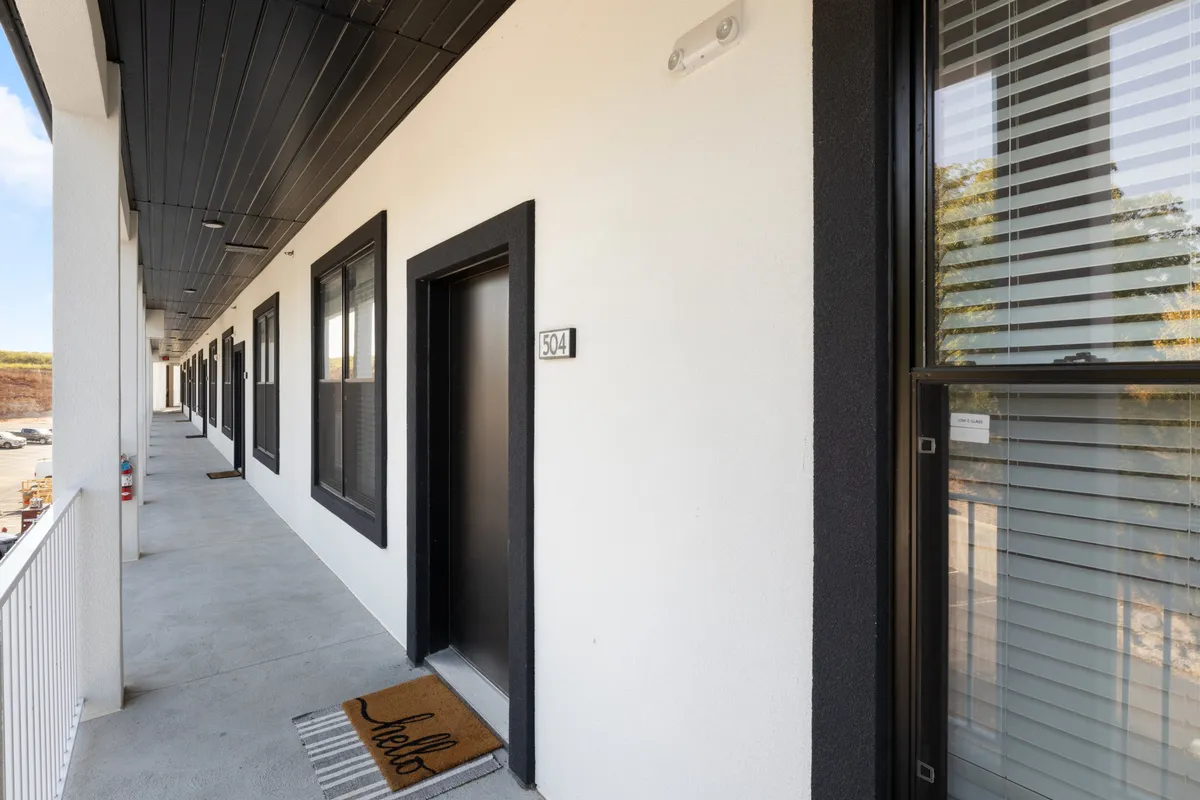An exterior entrance view showing the doorway with the unit number, a modern welcome mat, and windows with blinds, suggesting privacy and a contemporary vibe. The clean lines and welcoming feel set the tone for a high-end, thoughtfully managed property.