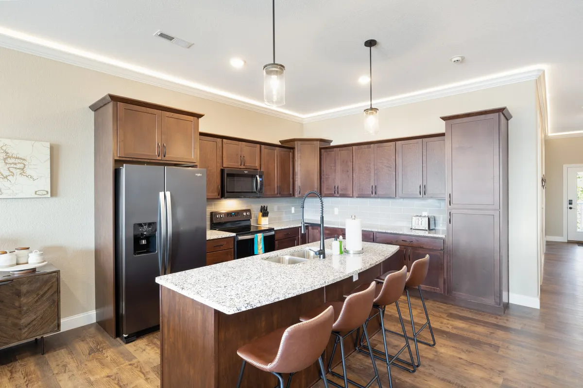 An inviting kitchen scene with a large granite kitchen island, modern bar stools, and a visible suite of stainless steel appliances. The space feels open and bright, encouraging shared meal prep and conversation. The kitchen exudes a welcoming and functional vibe, ideal for group cooking or enjoying coffee together.